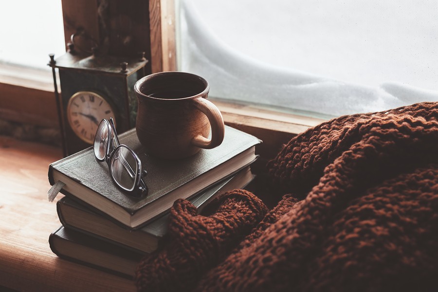 Warm and comfy winter concept. Book, cup of tea and sweater on wooden window sill in old house. Read